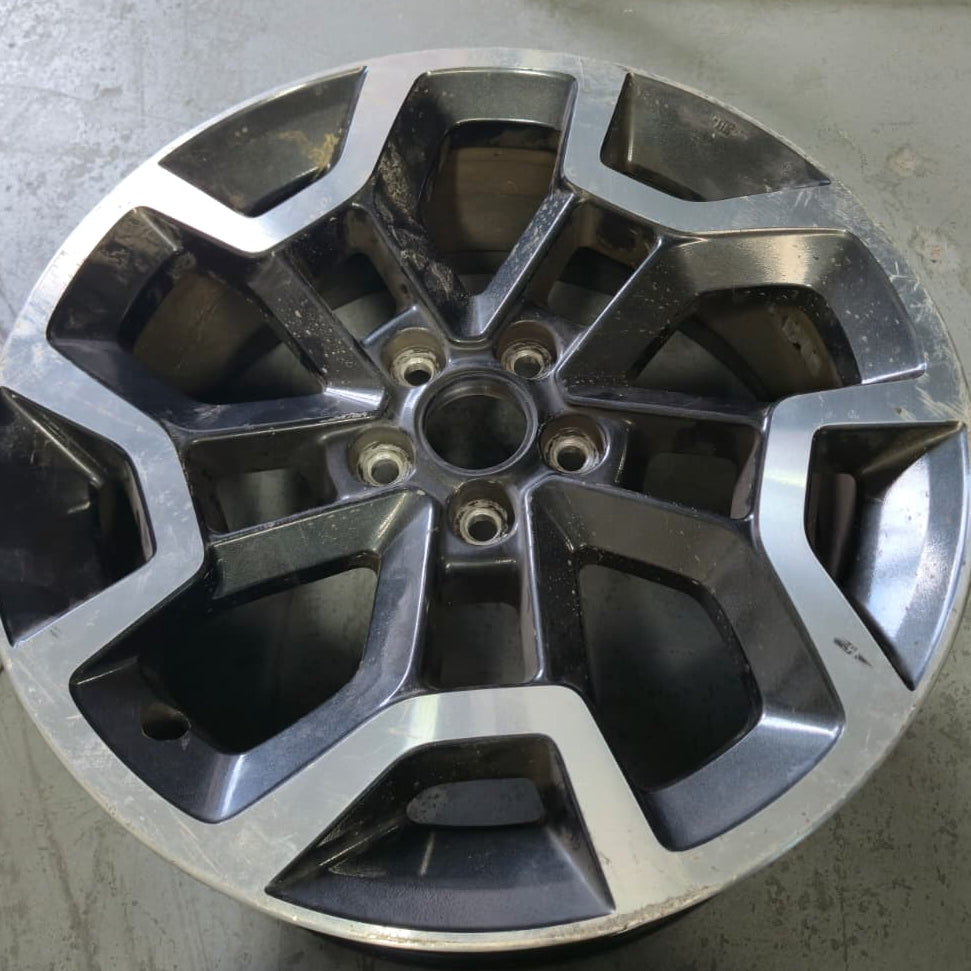 A multi-spoke alloy car wheel rim with a machined silver outer lip and dark gray inner sections, photographed on a concrete floor with other rims partially visible.