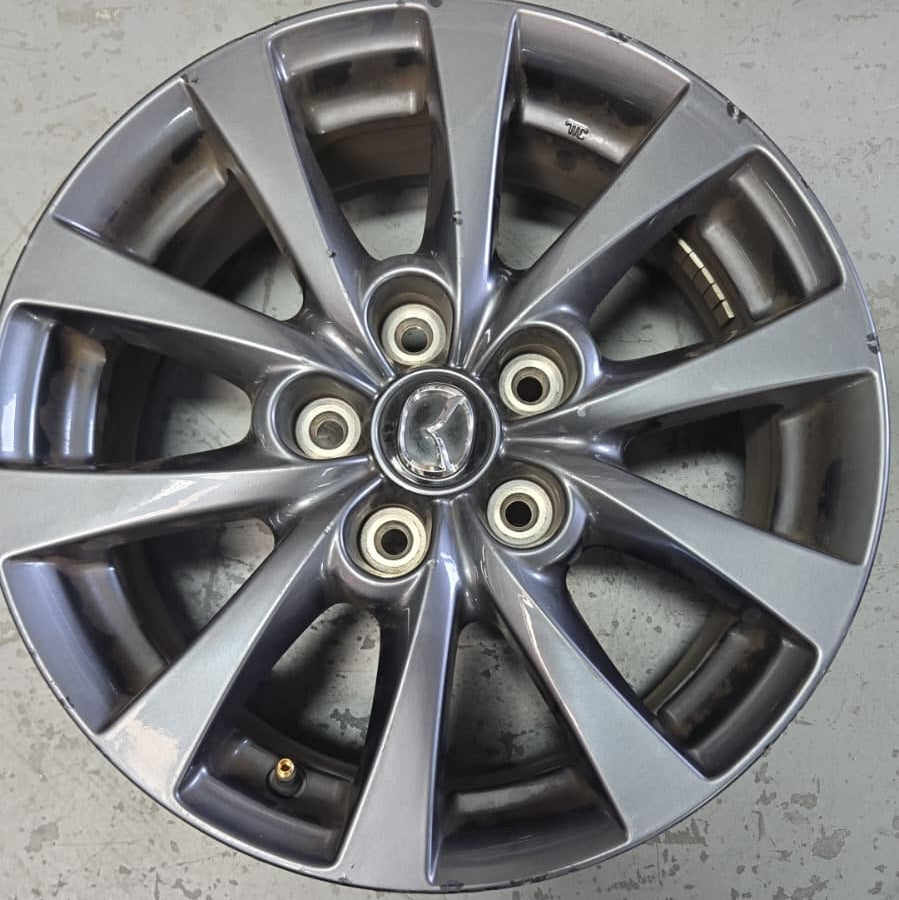 A silver metallic multi-spoke alloy wheel rim with a central Mercedes-Benz logo, photographed on a gray concrete floor.