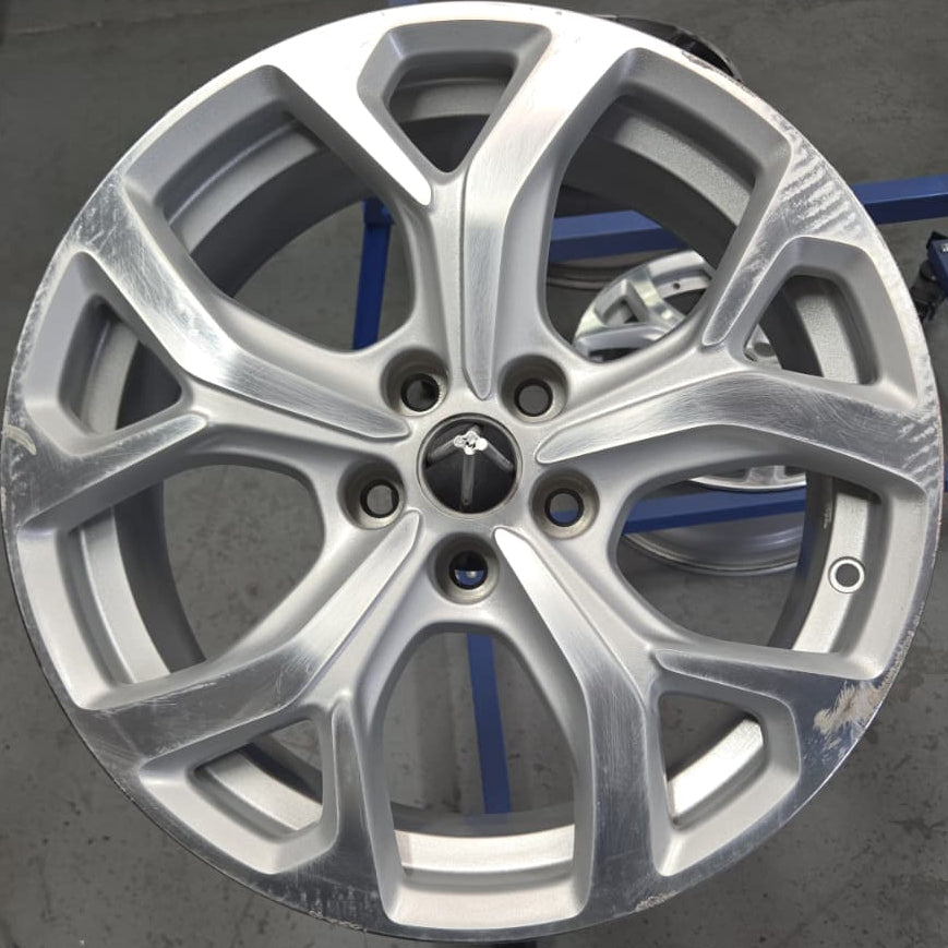 A silver multi-spoke alloy car wheel rim displayed on a stand in a workshop or garage setting.