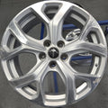 A silver multi-spoke alloy car wheel rim displayed on a stand in a workshop or garage setting.