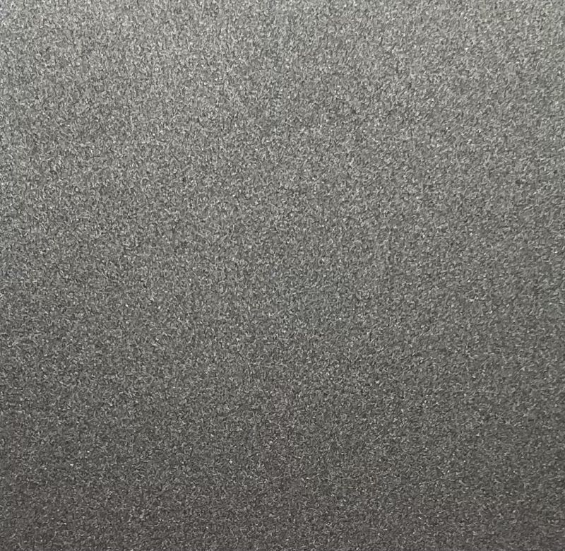 A close-up texture of a dark gray, metallic, granular material with a fine, sparkly surface.