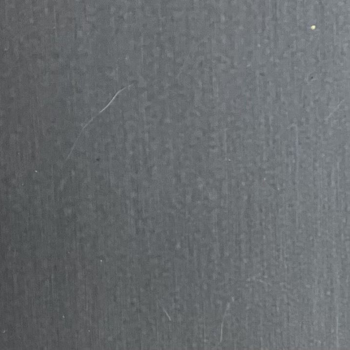 A close-up of a dark gray textured surface with fine vertical striations and a few small visible scratches.