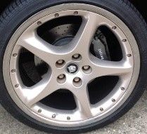 A close-up of a silver multi-spoke alloy wheel with a black tire, showing the center cap and brake assembly.