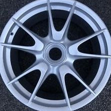 A silver multi-spoke alloy wheel rim photographed from a direct front angle on a dark textured surface.