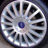A close-up of a silver multi-spoke alloy wheel with a blue Ford logo badge in the center, mounted on a black tire.