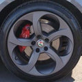 Car wheel with red brake caliper and Alfa Romeo logo on a black rim.