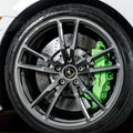 Close-up of a car wheel featuring a silver multi-spoke alloy rim, a black tire, a silver drilled brake disc, and a bright green Lamborghini brake caliper with the brand name visible.