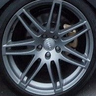 A close-up of a multi-spoke silver alloy car wheel with a dark tire and a visible brake disc.
