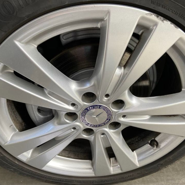 A close-up of a silver Mercedes-Benz alloy wheel with a visible brake rotor and tire, photographed outdoors on a concrete surface.