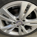 A close-up of a silver Mercedes-Benz alloy wheel with a visible brake rotor and tire, photographed outdoors on a concrete surface.