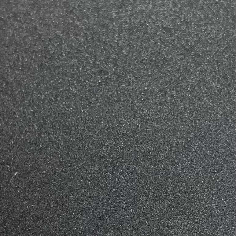 A close-up texture shot of a dark gray, granular material such as sand, gravel, or textured foam.