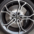 Close-up of a car wheel featuring a multi-spoke silver and black alloy rim, a silver ventilated brake disc, and a black brake caliper with visible Brembo branding.
