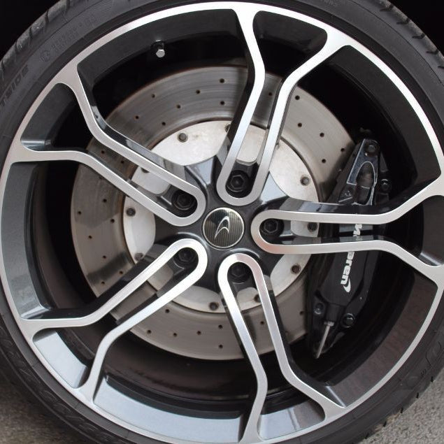 Close-up of a car wheel featuring a multi-spoke silver and black alloy rim, a silver ventilated brake disc, and a black brake caliper with visible Brembo branding.