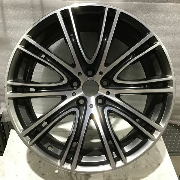 A multi-spoke alloy car wheel rim with a polished silver outer lip and a dark gray machined center, photographed against a gray textured background.